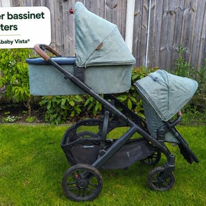 May include: A black UPPAbaby Vista stroller frame with upper bassinet adapters, featuring a sage green bassinet on top and a matching sage green seat below. The text "Upper bassinet adapters for UPPAbaby Vista" is visible in the upper left corner.