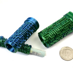 May include: Three 3D-printed cylindrical containers with a maze-like design in shades of blue and green. One container holds a rolled-up bill. A coin is next to the containers. The objects are on a white surface.