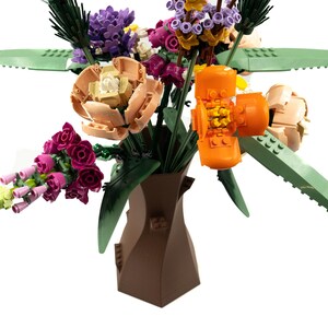Peut inclure: Un vase en c&eacute;ramique brun &agrave; la forme unique contient un bouquet de fleurs color&eacute;es. Le bouquet comprend des fleurs roses, violettes, orange et p&ecirc;che avec des feuilles vertes.
