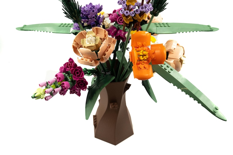 Peut inclure: Un vase en c&eacute;ramique brun &agrave; la forme unique contient un bouquet de fleurs color&eacute;es. Le bouquet comprend des fleurs roses, violettes, orange et p&ecirc;che avec des feuilles vertes.