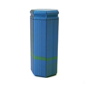 May include: A blue, hexagonal-shaped container with a matching lid. The container has a textured surface and a green stripe around the middle. The design is reminiscent of a pillar or column.