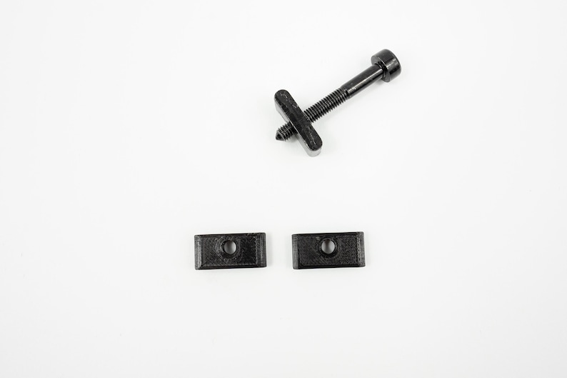 May include: A set of three black plastic hardware pieces, including a screw with a head and two rectangular plates with holes.