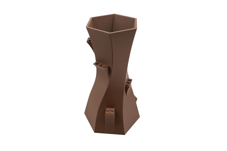 Peut inclure: Un vase en c&eacute;ramique brun avec un design unique et torsad&eacute;. Le vase a une ouverture hexagonale en haut et une base large.