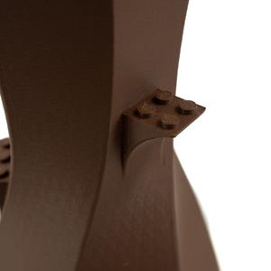 Peut inclure: Un vase en c&eacute;ramique brun au design moderne et unique. Le vase a une surface textur&eacute;e et pr&eacute;sente une petite ouverture carr&eacute;e en haut. Le vase est d&eacute;cor&eacute; d'une petite pi&egrave;ce en plastique de type Lego brune sur le c&ocirc;t&eacute;.