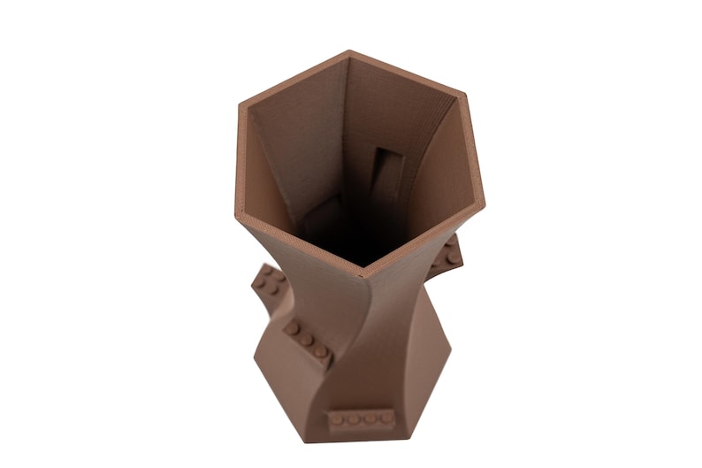 Peut inclure: Un vase en c&eacute;ramique brun avec un design g&eacute;om&eacute;trique unique. Le vase a une ouverture hexagonale et une forme torsad&eacute;e en sablier.