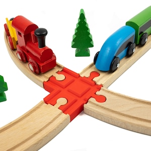 May include: A wooden toy train set with a red engine, a blue car, and a green car. The train tracks are made of wood and have a red and white puzzle piece connector. There are two green wooden trees.