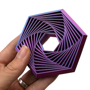 Puede incluir: Una forma hexagonal geométrica de color morado y azul, hecha de metal superpuesto. El hexágono es un diseño en espiral con un agujero en el centro.