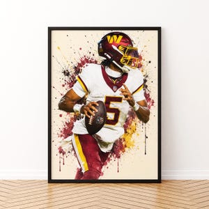 May include: A framed art print featuring a football player in a white and burgundy uniform with the number 5, wearing a matching helmet, holding a football. The design includes dynamic burgundy and yellow paint splatter effects on a cream background.