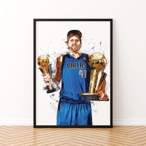 May include: A basketball player wearing a blue jersey with "Dallas 41" on the front, holding two gold championship trophies. The player is standing against a white background with splashes of paint.