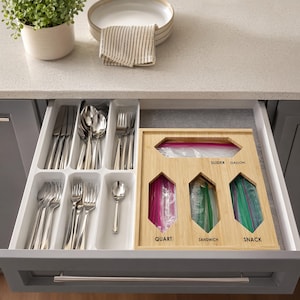May include: A kitchen drawer organizer set featuring a white plastic tray with multiple compartments for silverware and a light wood bamboo storage box with labeled slots for gallon, quart, sandwich, and snack plastic storage bags.