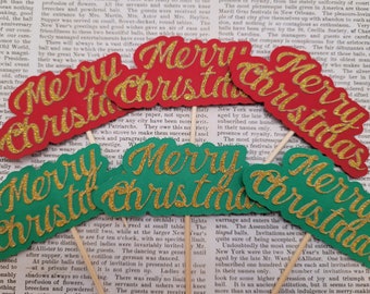 May include: Red and green "Merry Christmas" glitter cardstock cutouts on wooden sticks. Festive holiday decor for parties, events, or seasonal displays. The text is in a gold script font.