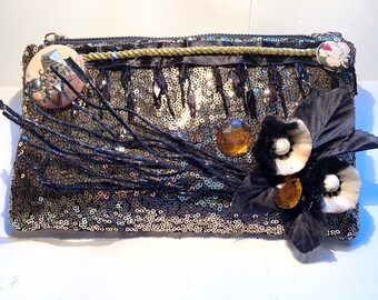 May include: A gold sequined clutch with black fringe, black fabric flowers, and gold and clear rhinestones.