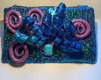 May include: A blue sequined clutch with pink and blue ribbon embellishments and a turquoise stone accent.
