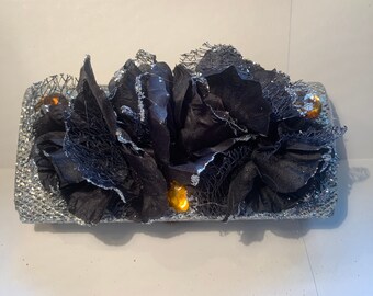 May include: A silver glitter clutch with black fabric flowers and gold rhinestones.