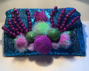 May include: A blue sequined clutch purse with purple and green pom-poms and beads.