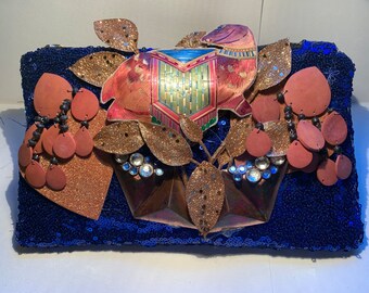 May include: A blue sequined clutch with gold glitter and embellishments. The clutch features a pink and gold animal design with a floral motif.