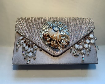 May include: A silver clutch purse with a beaded fringe and a shell embellishment. The shell is surrounded by brown and white beads.