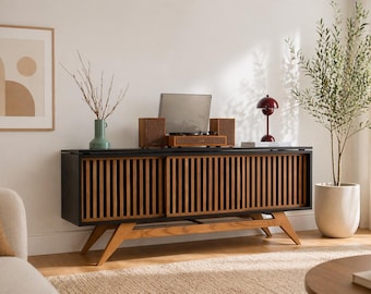 May include: A mid-century modern style entertainment center with a black top and slatted wooden doors. A record player with speakers sits on top, along with a red lamp and a green vase. A framed abstract art piece and a potted plant are also in the room.