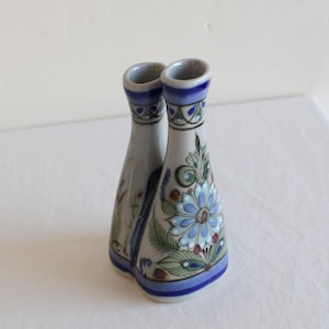 May include: A ceramic vase with two connected chambers. The vase is primarily light gray with blue and green floral designs. The rim and base are accented with blue bands. The design includes a large blue flower.