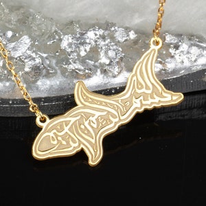 Op de afbeelding: Een gouden ketting met een hanger in de vorm van een haai. De haai is van goud en heeft Arabische kalligrafie in zijn lichaam gegraveerd.