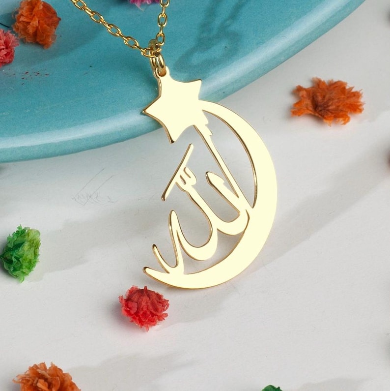 Peut inclure: Un collier pendentif en m&eacute;tal dor&eacute; repr&eacute;sentant un croissant de lune int&eacute;gr&eacute; &agrave; une &eacute;toile &agrave; cinq branches sur le dessus. Le centre du croissant de lune pr&eacute;sente une calligraphie arabe. Le pendentif est suspendu &agrave; une fine cha&icirc;ne en m&eacute;tal dor&eacute;.