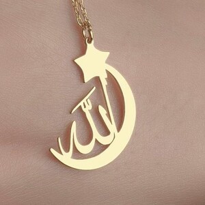 Peut inclure: Un collier dor&eacute; avec un pendentif en forme de croissant de lune et d'&eacute;toile &agrave; cinq branches. La calligraphie arabe pour Allah est int&eacute;gr&eacute;e au centre du design en croissant de lune, suspendu &agrave; une fine cha&icirc;ne de couleur dor&eacute;e.