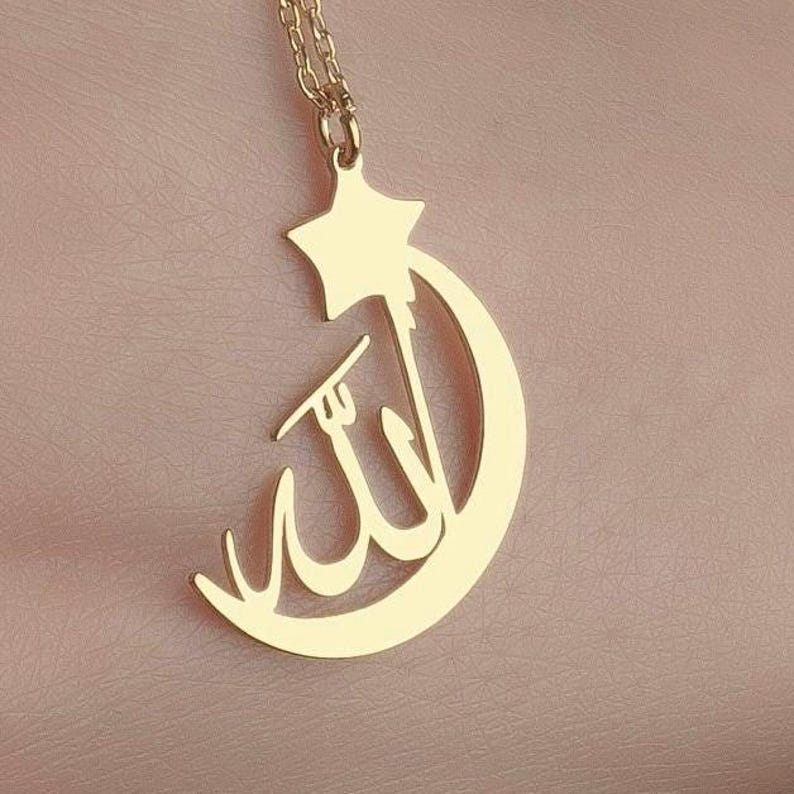 Peut inclure: Un collier dor&eacute; avec un pendentif en forme de croissant de lune et d'&eacute;toile &agrave; cinq branches. La calligraphie arabe pour Allah est int&eacute;gr&eacute;e au centre du design en croissant de lune, suspendu &agrave; une fine cha&icirc;ne de couleur dor&eacute;e.