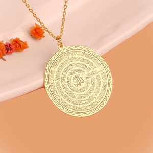 Pu&ograve; includere: Una collana con ciondolo circolare color oro caratterizzata da un'intricata calligrafia araba incisa a spirale. Il centro del disco mostra la parola Allah, circondata da linee di testo concentriche e da un bordo decorativo lungo il perimetro.