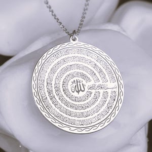 Pu&ograve; includere: Un ciondolo circolare color argento con un'intricata calligrafia araba incisa a spirale. Il centro mostra la parola Allah, circondata da linee di testo concentriche, rifinito con un bordo intrecciato decorativo.
