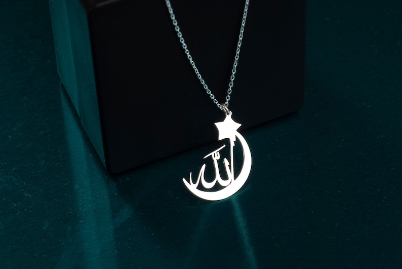 Peut inclure: Un collier de couleur argent&eacute;e avec un pendentif en forme de croissant de lune et d'&eacute;toile. Le croissant de lune contient la calligraphie arabe pour Allah. Le pendentif est suspendu &agrave; une d&eacute;licate cha&icirc;ne &agrave; maillons argent&eacute;e.