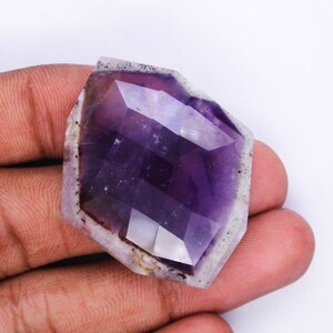 Pu&ograve; includere: Un cristallo di ametista sfaccettato con una tonalit&agrave; viola e un esterno bianco nuvoloso. Il cristallo ha la forma di un esagono e una superficie liscia e lucida.
