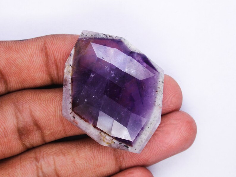 Pu&ograve; includere: Un cristallo di ametista sfaccettato con una tonalit&agrave; viola e un esterno bianco nuvoloso. Il cristallo ha la forma di un esagono e una superficie liscia e lucida.