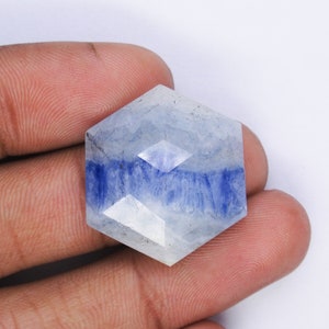 May include: A hexagonal blue and white gemstone with a faceted cut. The gemstone has a cloudy white appearance with blue streaks throughout.