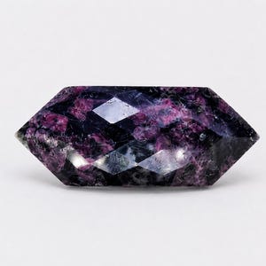 May include: A faceted, marquise-shaped gemstone featuring a mottled pattern of deep purple, magenta, and black inclusions. The stone has a polished surface with multiple geometric facets that reflect light across its elongated, pointed ends.