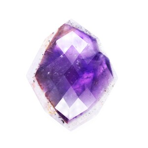 Pu&ograve; includere: Un cristallo di ametista viola con una forma geometrica sfaccettata. Il cristallo ha un aspetto chiaro e traslucido con un leggero luccichio.