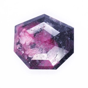 Könnte beinhalten: Ein facettierter Edelstein mit einem rosa-schwarzen Farbmuster. Der Edelstein ist in hexagonaler Form geschliffen.