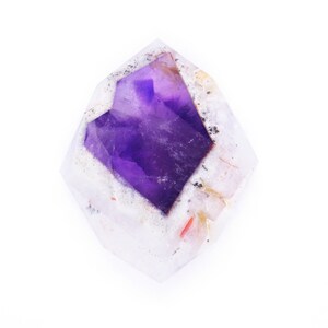 Pu&ograve; includere: Un cristallo di ametista viola con un esterno chiaro, bianco e rosa. Il cristallo ha la forma di una punta e una texture ruvida e naturale.