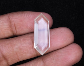 May include: A clear, faceted crystal pendant with a hexagonal shape. The crystal is held in a hand against a black background. The pendant is approximately 1.5 inches long.