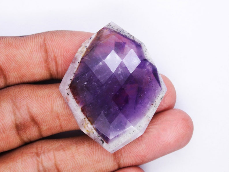 Pu&ograve; includere: Un grande gioiello di ametista sfaccettato con una tonalit&agrave; viola e un bordo bianco nuvoloso. Il gioiello &egrave; tagliato in una forma geometrica unica.
