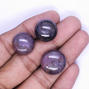 May include: Three round, polished cabochon gemstones with a smooth, domed surface. The stones exhibit a deep, translucent purple and dark violet color palette with visible internal inclusions and natural veining patterns throughout each piece.