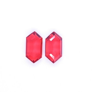 May include: Two faceted, red-colored, hexagonal-shaped gemstones. The gems are transparent and appear to be made of glass or crystal. They are set against a white background.