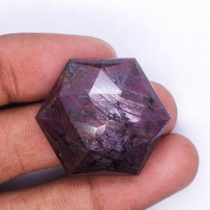 May include: A large, faceted, purple gemstone with a star-shaped cut. The gemstone has a dark purple hue with black inclusions.