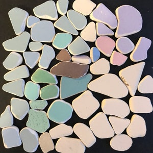 May include: A selection of sea glass fragments in pastel hues, such as blue, green, pink, and white. The pieces have smooth, rounded edges and are displayed on a black background. The sea glass pieces vary in shape and size.