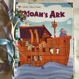 May include: A Little Golden Book titled "Noah's Ark" with a colorful illustration of the ark, animals, and the biblical story. The book is bound with decorative ribbons in pastel colors and a charm.