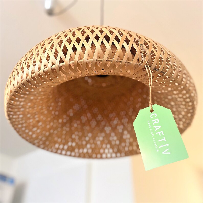 May include: A woven bamboo pendant light fixture with a natural finish. The light has a rounded, open-weave design and a tag that reads "CRAFTIV hand craft creative". The light is suspended from the ceiling.