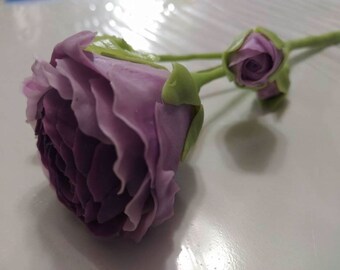 May include: Two purple artificial flowers with green stems and leaves. The larger flower is fully bloomed and the smaller flower is a bud.