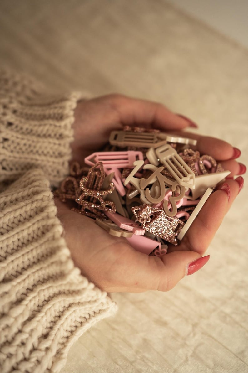 May include: A handful of pink and gold glitter hair clips, including a few shaped like pencils and letters.