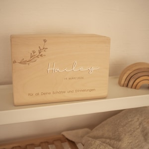 Puede incluir: Una taza de cerámica blanca con un asa negra y el texto "But First, Coffee" en negrita negra. La taza está sobre una superficie de madera. La taza mide aproximadamente 10 cm de alto.