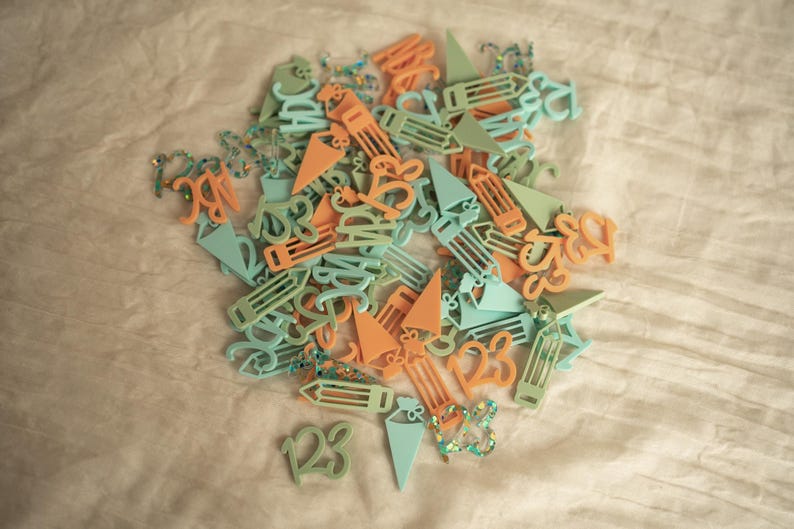 May include: A pile of colorful plastic shapes, including numbers, letters, and pencils, in shades of light blue and orange. The shapes are scattered on a light beige surface.