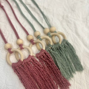 May include: Four handmade macrame wall hangings with wooden rings and tassels. Two are in a dusty rose color and two are in a sage green color.